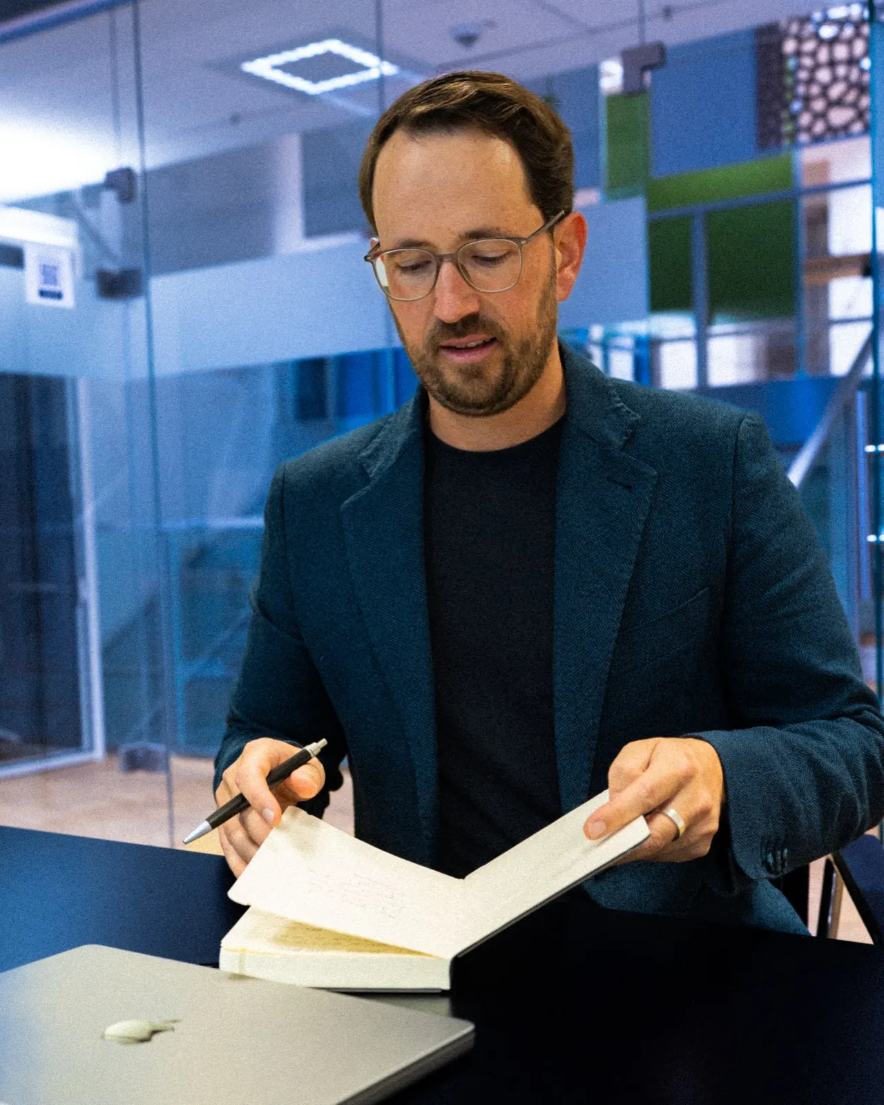 Bernhard Neumann arbeitet mit Stift und Notizbuch am Schreibtisch