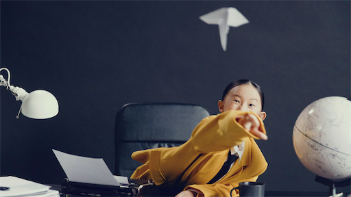 Mädchen im gelben Anzug wirft einen Papierflieger